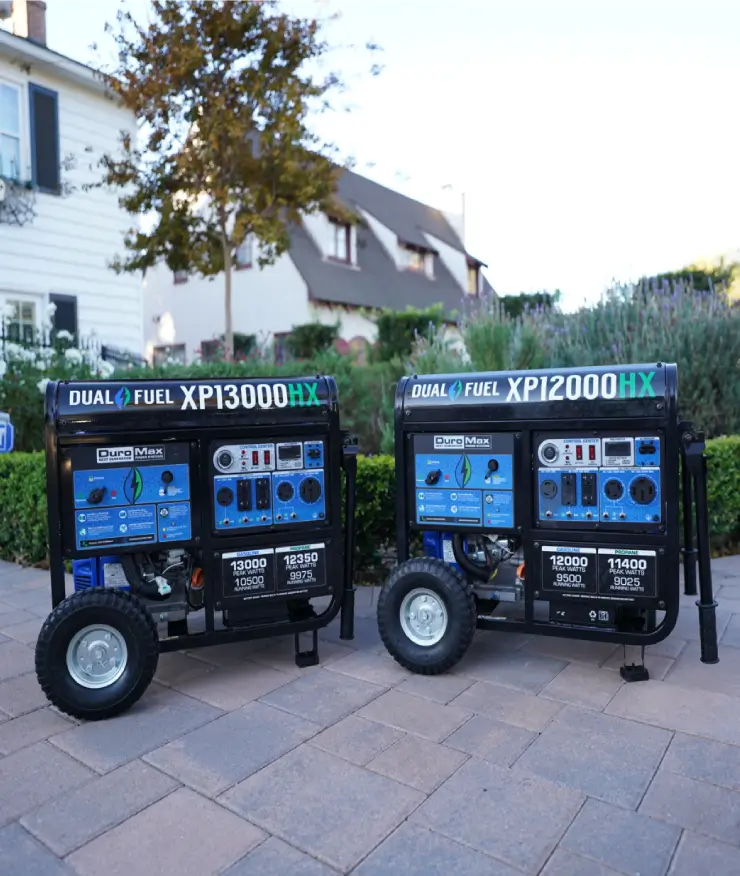 Two generators are parked on the sidewalk outside a house.